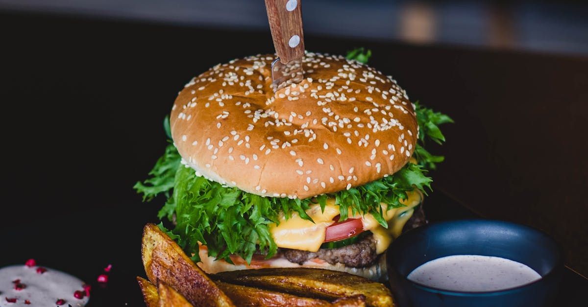 Hamburger with sesame seed bun, lettuce, cheese, and a steak knife; served with fries and a dipping sauce.