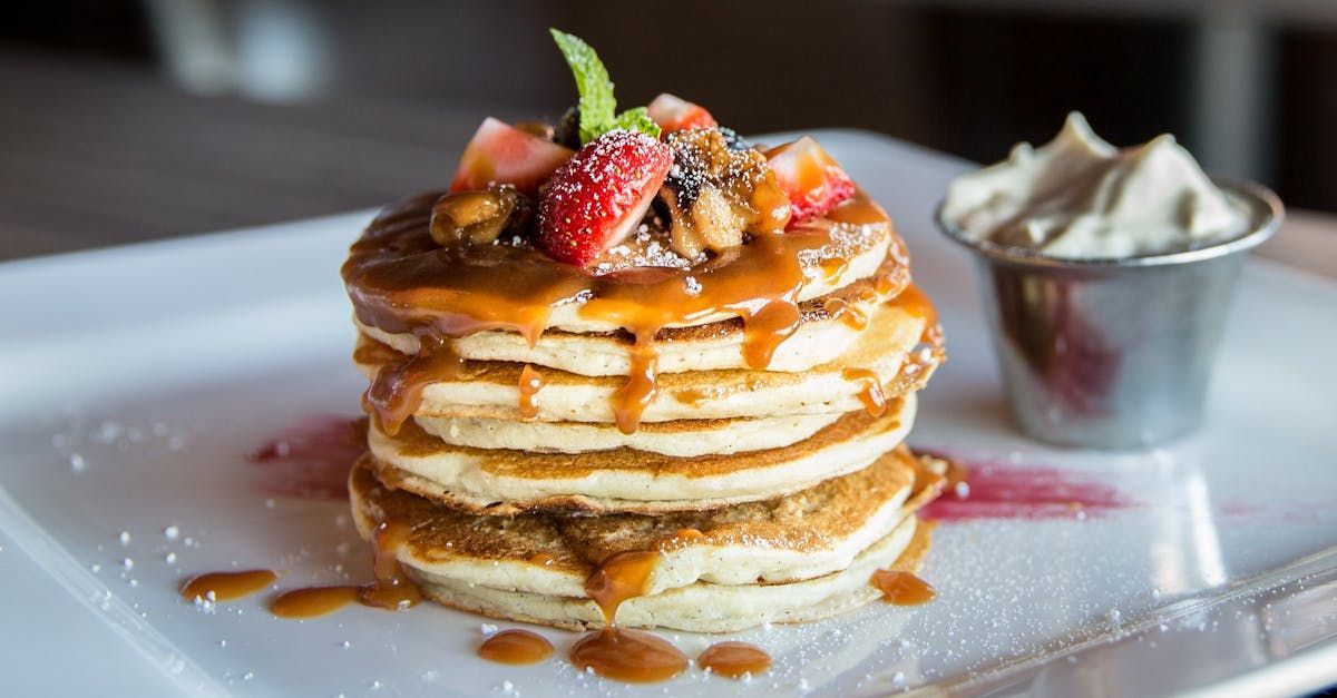 Stack of pancakes with caramel sauce, strawberries, nuts, and whipped cream.