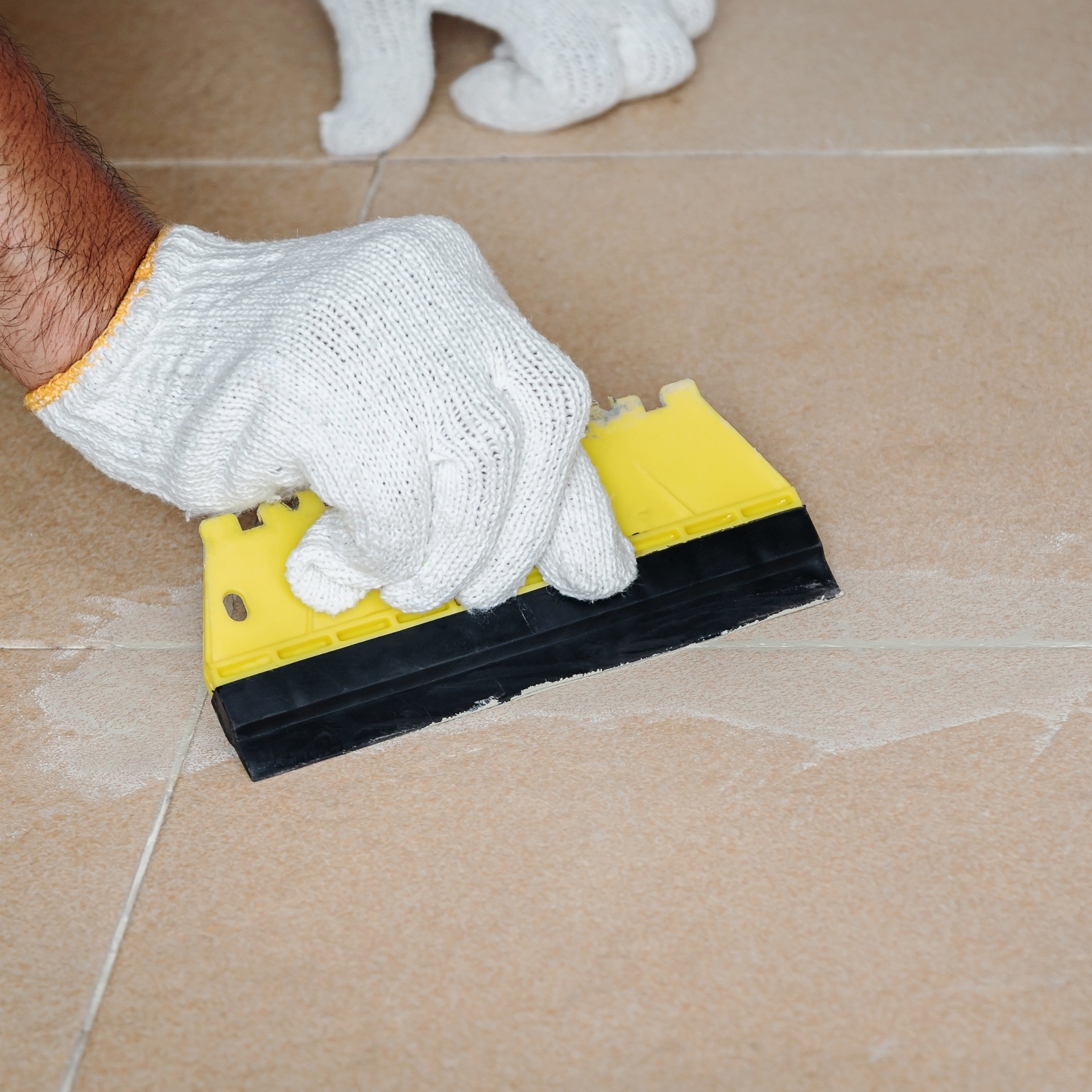 Eco Friend Carpet Clean - Person in gloves using a yellow and black grout float to fill grout lines on tile.