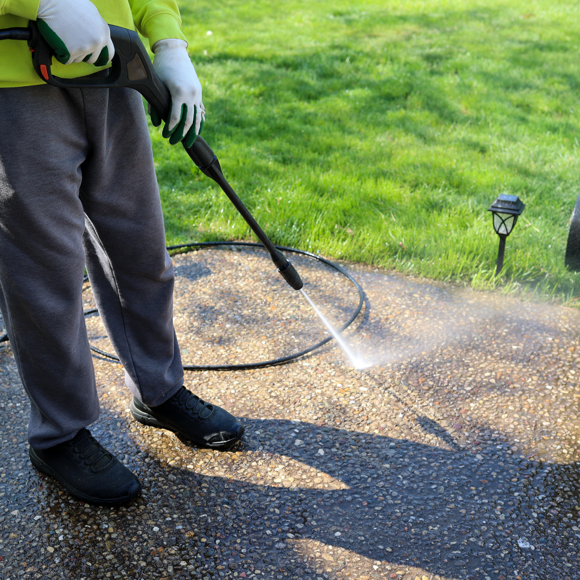 Eco Friend Carpet Clean - Person wearing gloves pressure washing a dark concrete sidewalk.