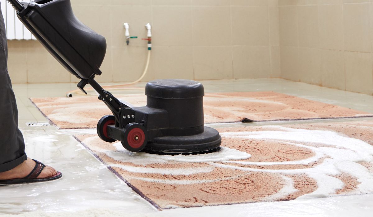 Eco Friend Carpet Clean - Person using a floor buffer to clean a rug with soapy water in a room.