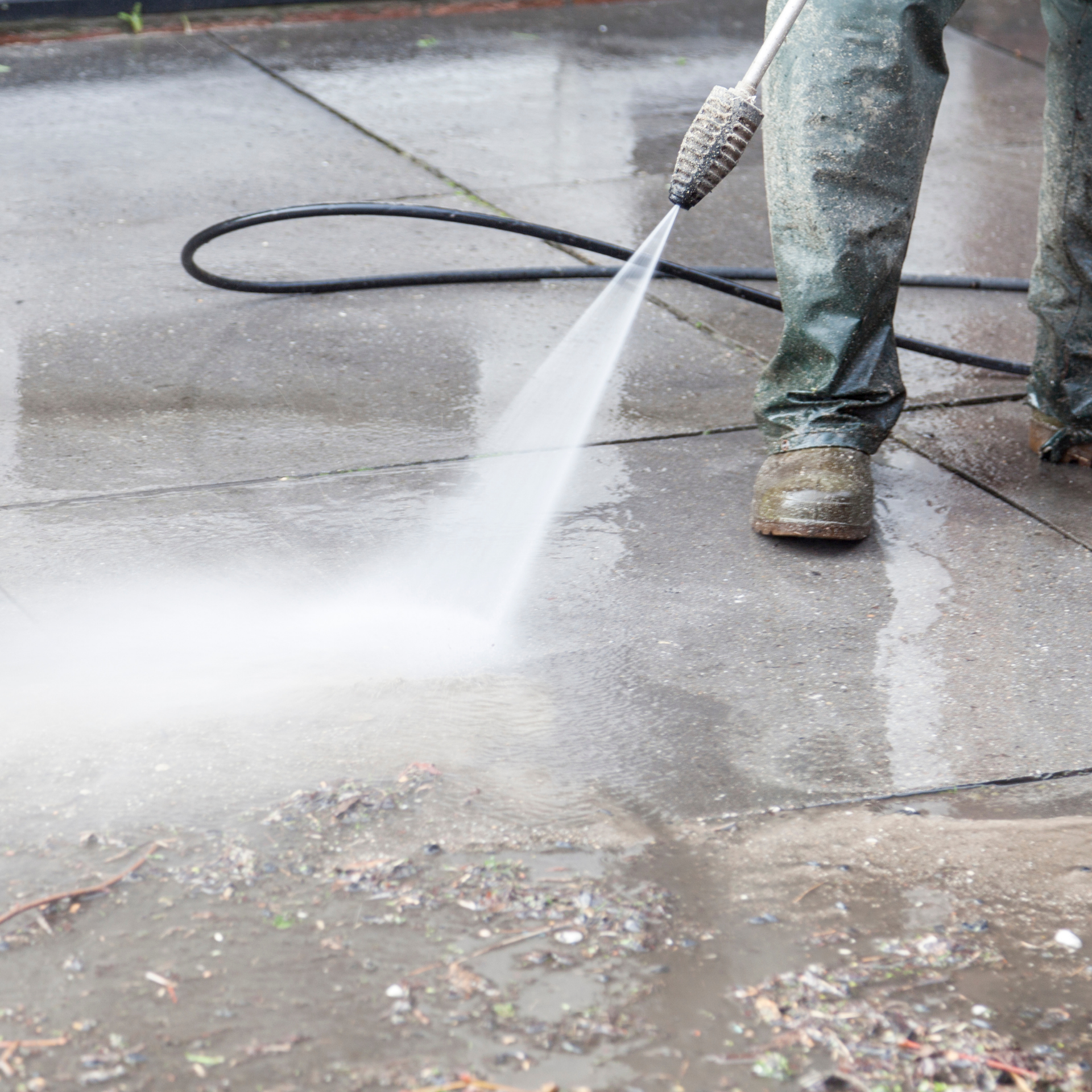 Eco Friend Carpet Clean - Person in work clothes power washing a gray concrete surface with muddy water.