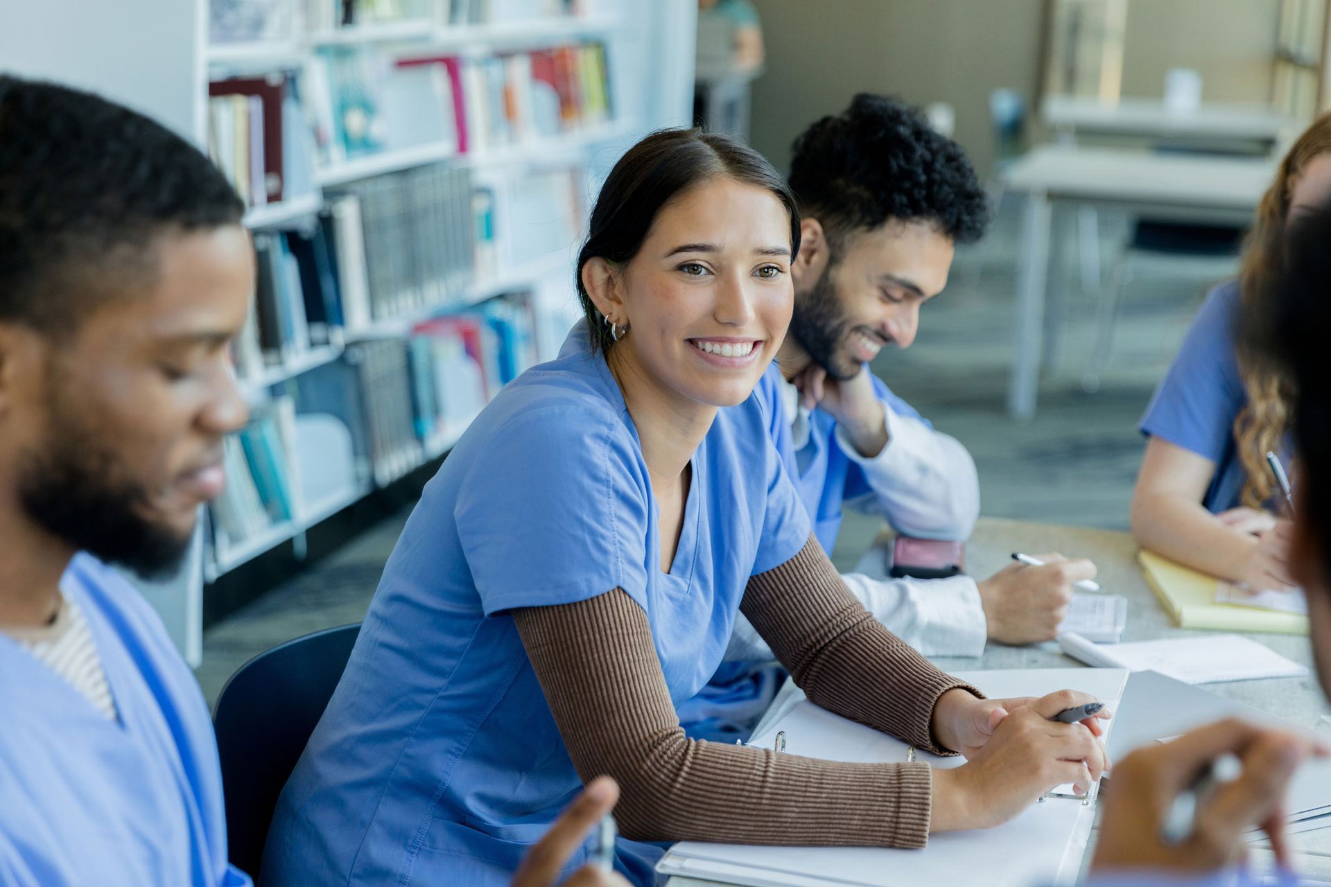 A group of nurses are sitting at a table in a library.