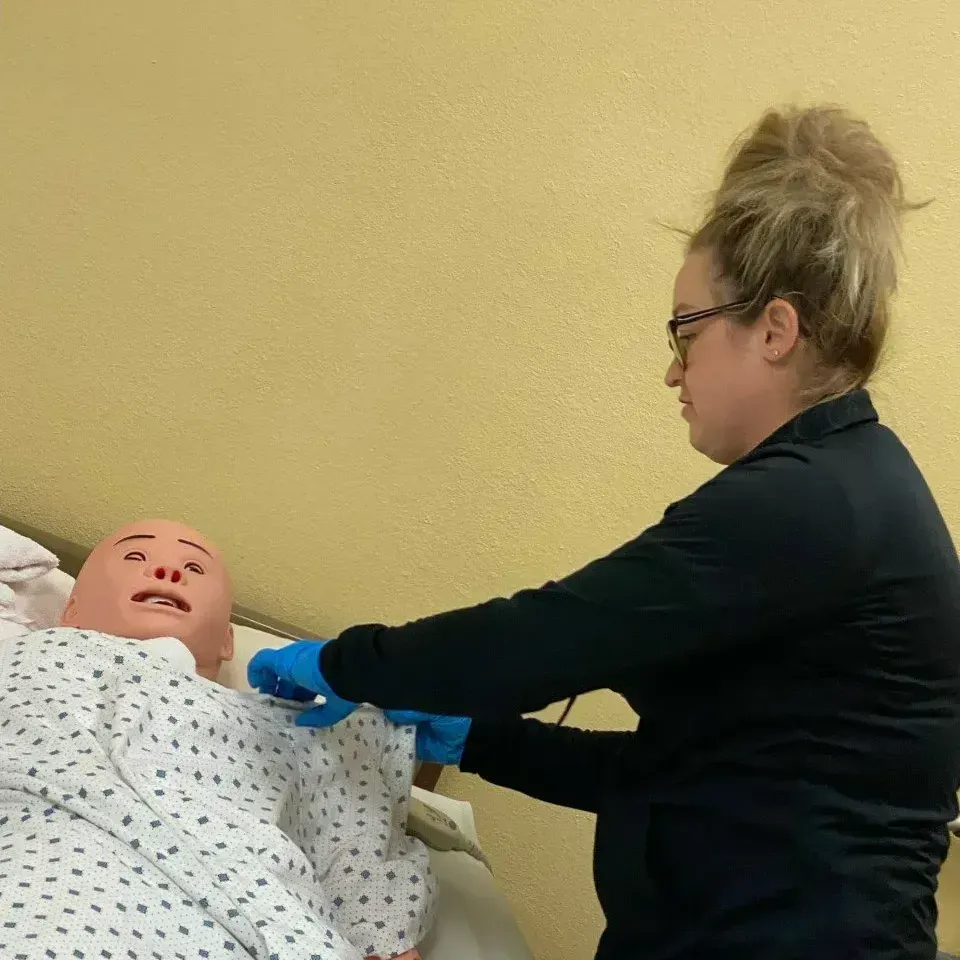 A woman is working on a mannequin in a hospital bed