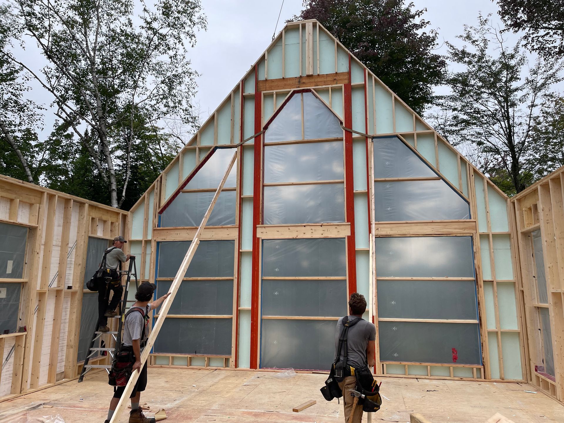 Construction de l'intérieur d'un bâtiment en bois. Des ouvriers construisent les murs autour de grandes fenêtres, laissant apparaître l'isolation.
