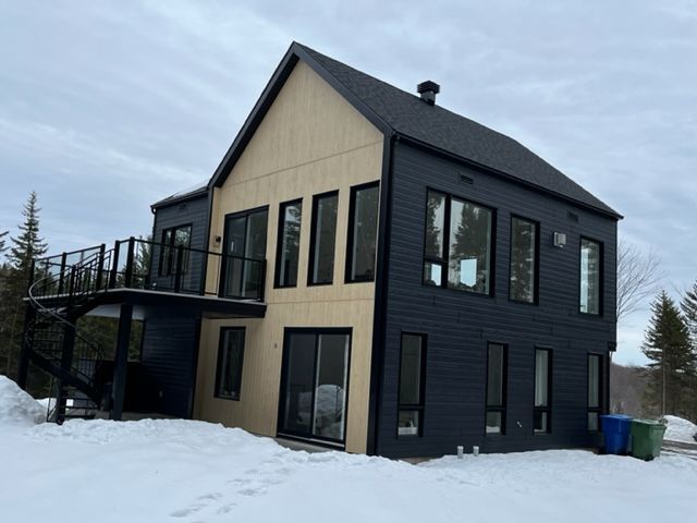 Maison moderne à deux étages avec bardage noir et lambris clair, cour enneigée et balcon.