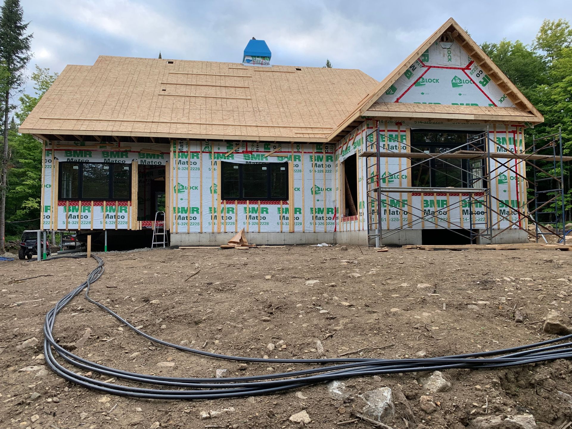 Une maison en construction. Les murs extérieurs sont recouverts, les fenêtres sont installées et le toit est partiellement recouvert de bardeaux.