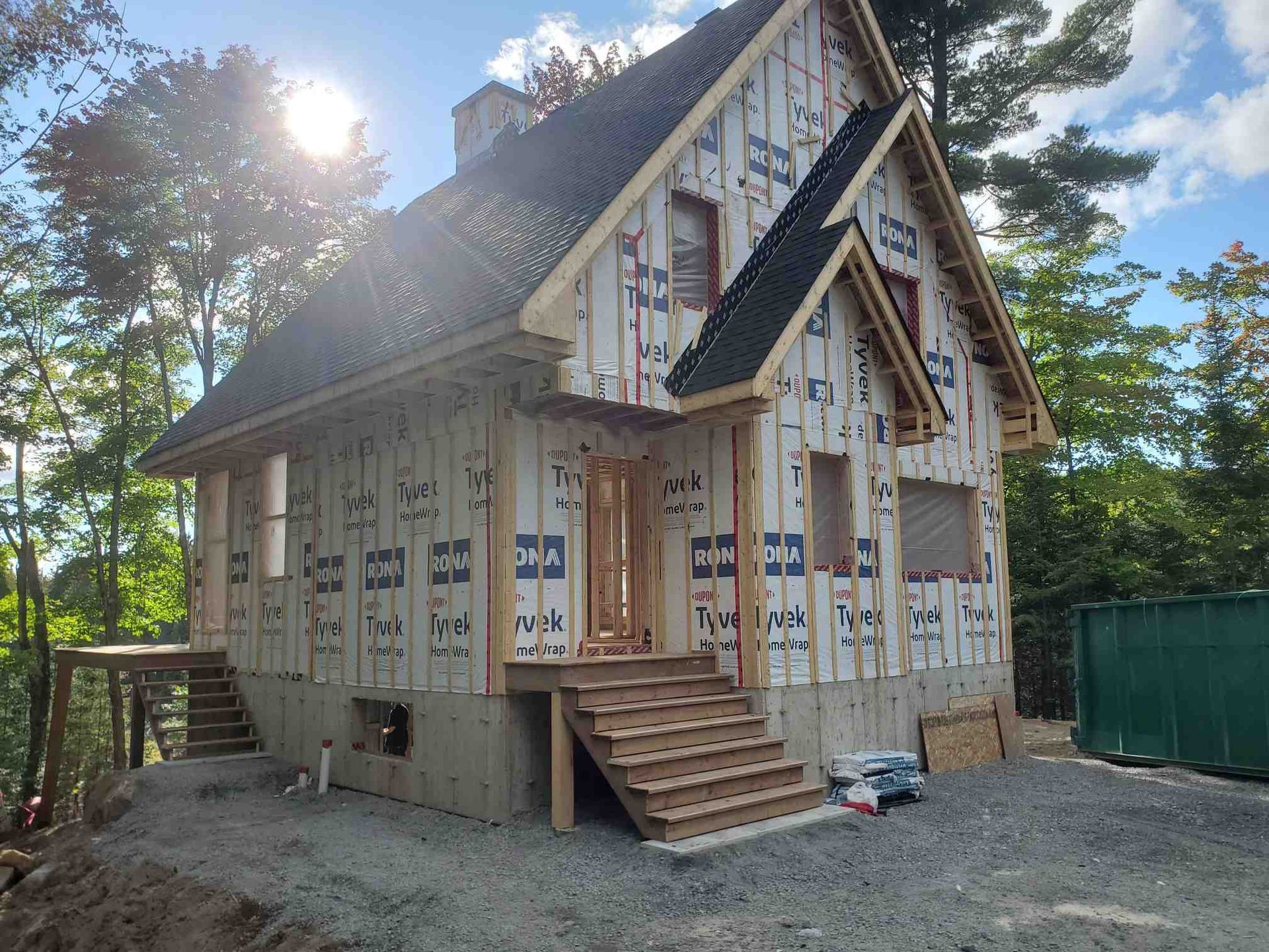 Cabane en construction avec charpente en bois, toit foncé et recouverte d'une bâche résistante aux intempéries.