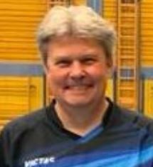 Ein Mann in einem schwarz - blauen Hemd lächelt in die Kamera.