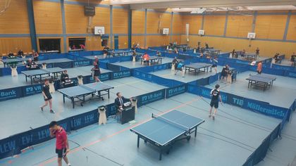 Eine Gruppe von Leuten spielt in einer großen Turnhalle Tischtennis.