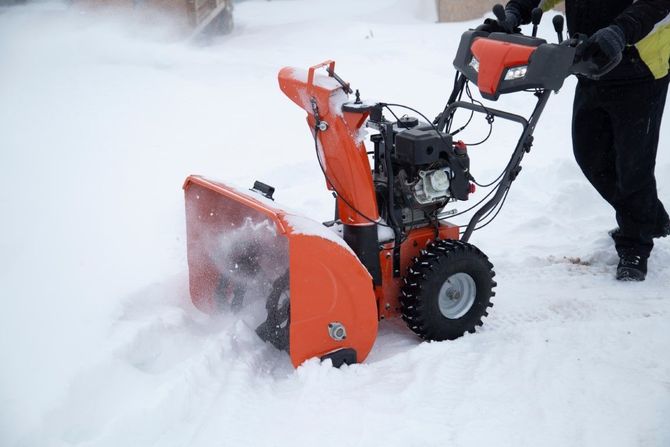 Orange snow blower clearing deep snow as a person operates it outdoors