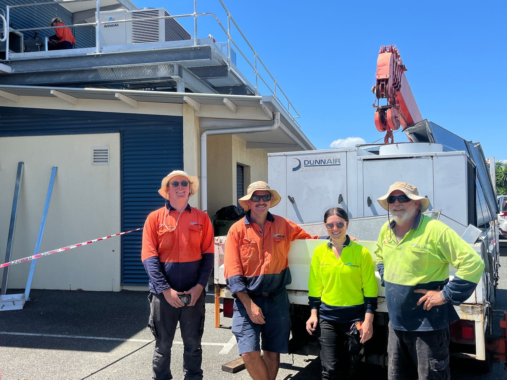 Four workers in high-visibility clothing stand outside a building near a truck-mounted crane. — Depinto Agencies In North Mackay, QLD