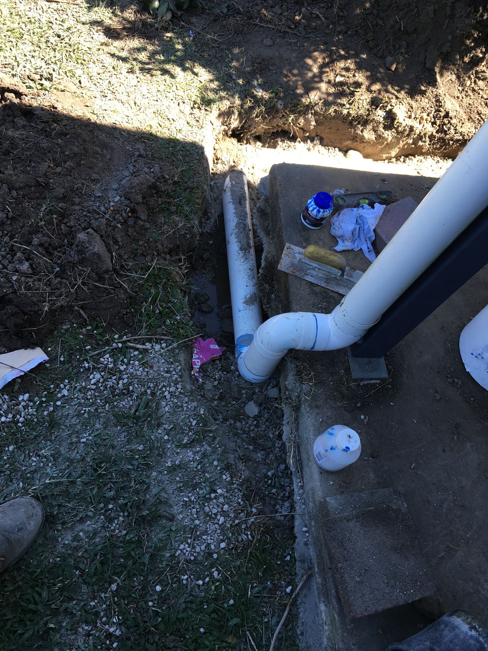 Outdoor utility area with white drainage pipe beside concrete steps and gravel, showing a small blue object nearby — Depinto Agencies In North Mackay, QLD