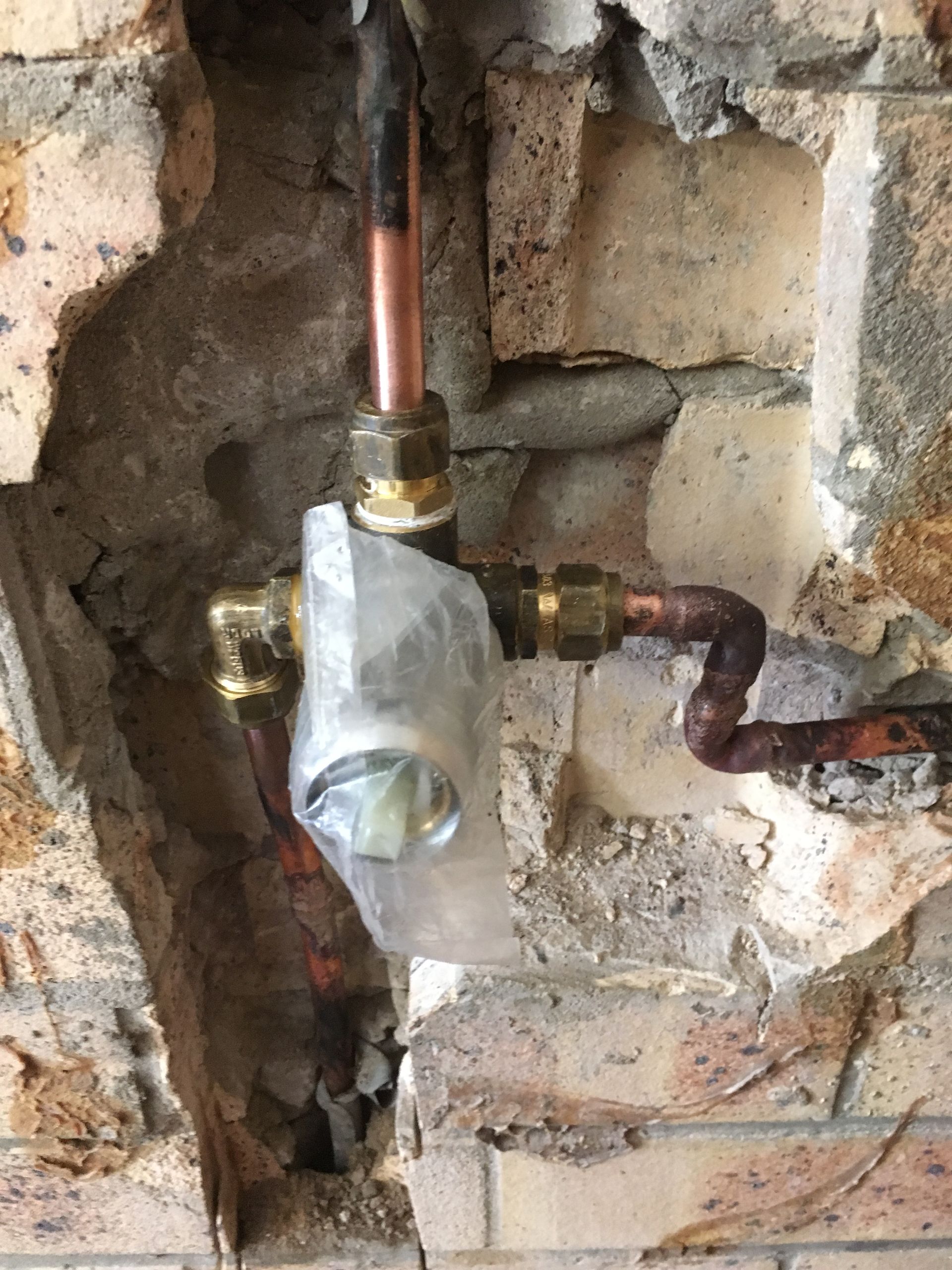 Exposed copper plumbing valve and pipes set into a rough brick wall opening — Depinto Agencies In North Mackay, QLD