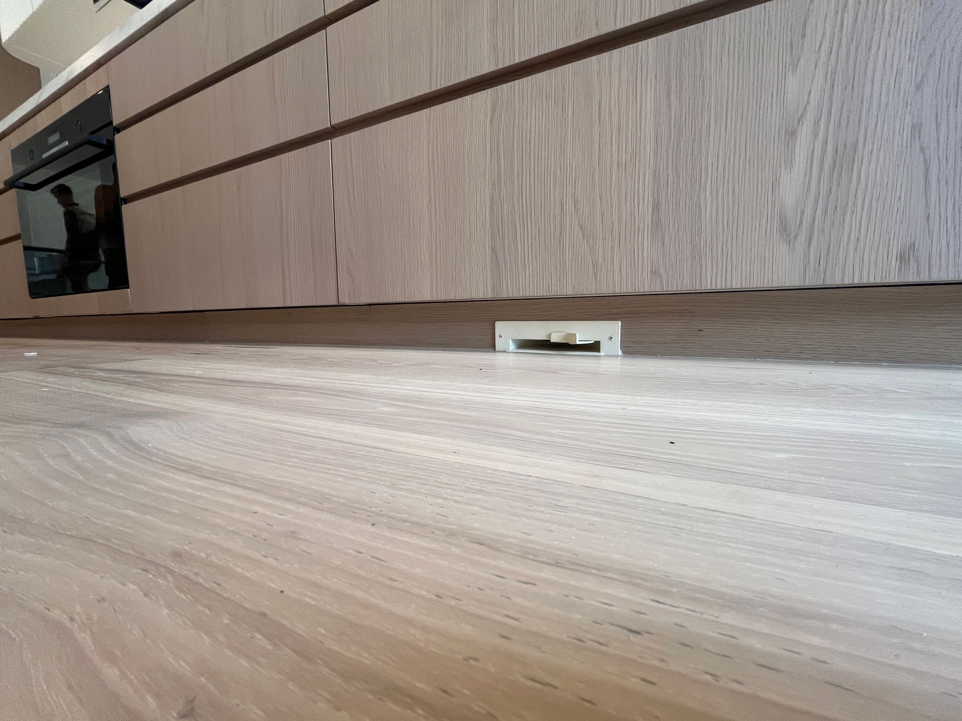 Low-angle view under a wooden cabinet with a small white floor mount or bracket on the floor — Depinto Agencies In North Mackay, QLD