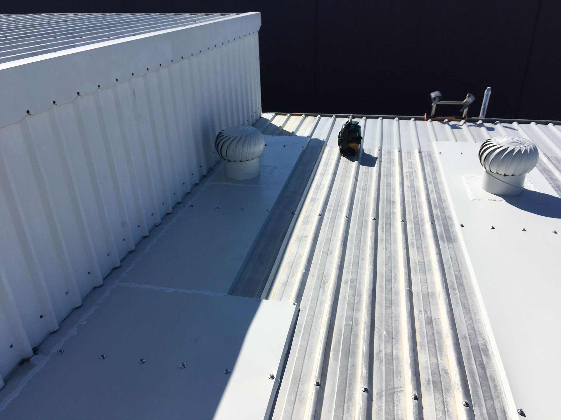 White metal rooftop with vents, skylights, and bright sunlight casting shadows. — Depinto Agencies In North Mackay, QLD