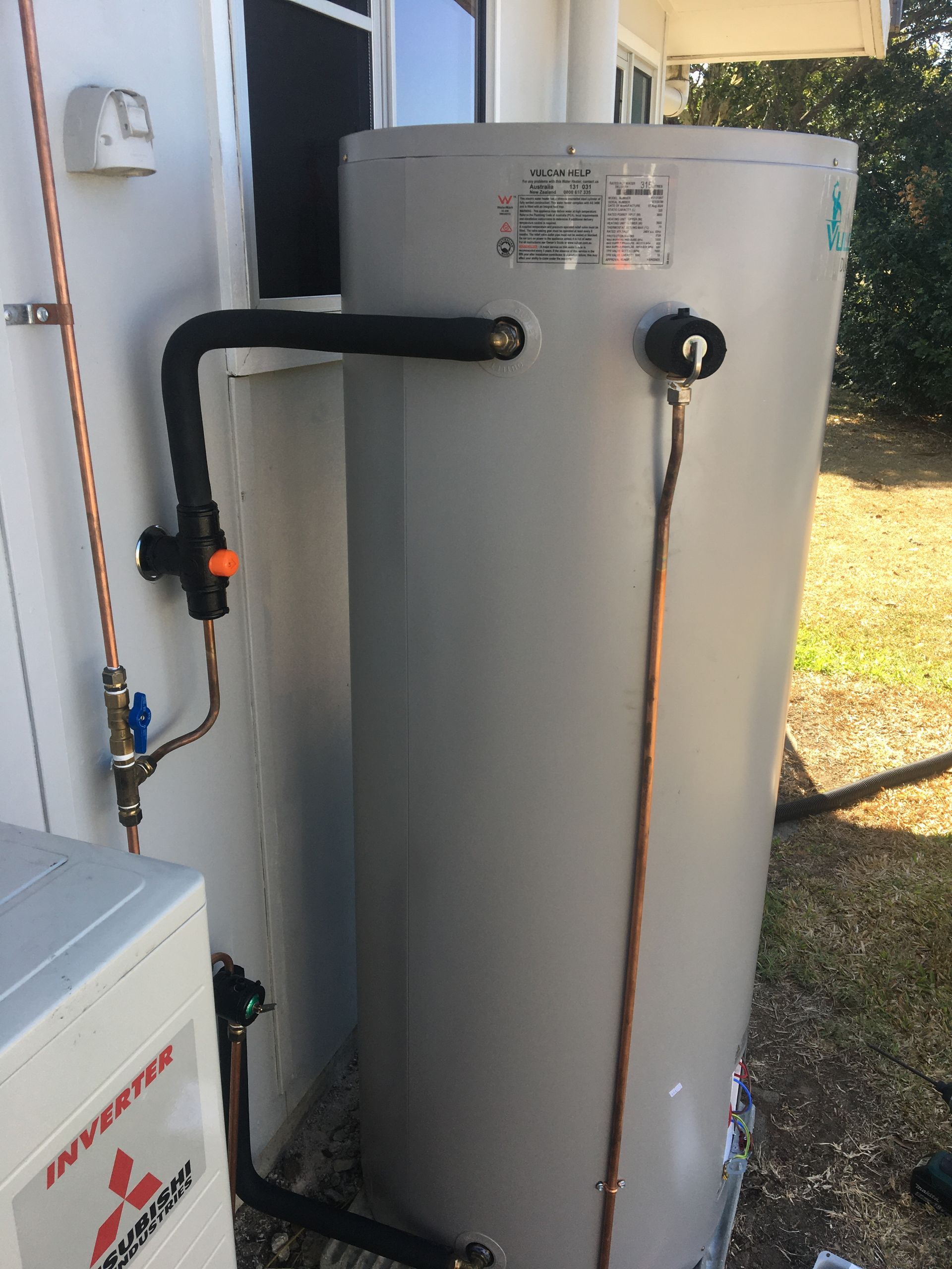 Gray water heater tank with connected black and copper pipes beside a house exterior — Depinto Agencies In North Mackay, QLD
