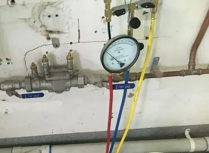 Plumbing manifold with pressure gauge and red, blue, and yellow hoses against a white wall — Depinto Agencies In North Mackay, QLD