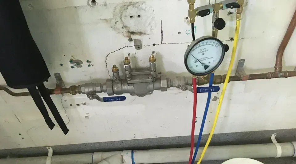 Plumbing pipes with a pressure gauge and red, blue, and yellow hoses on a wall above a sink basin — Depinto Agencies In North Mackay, QLD