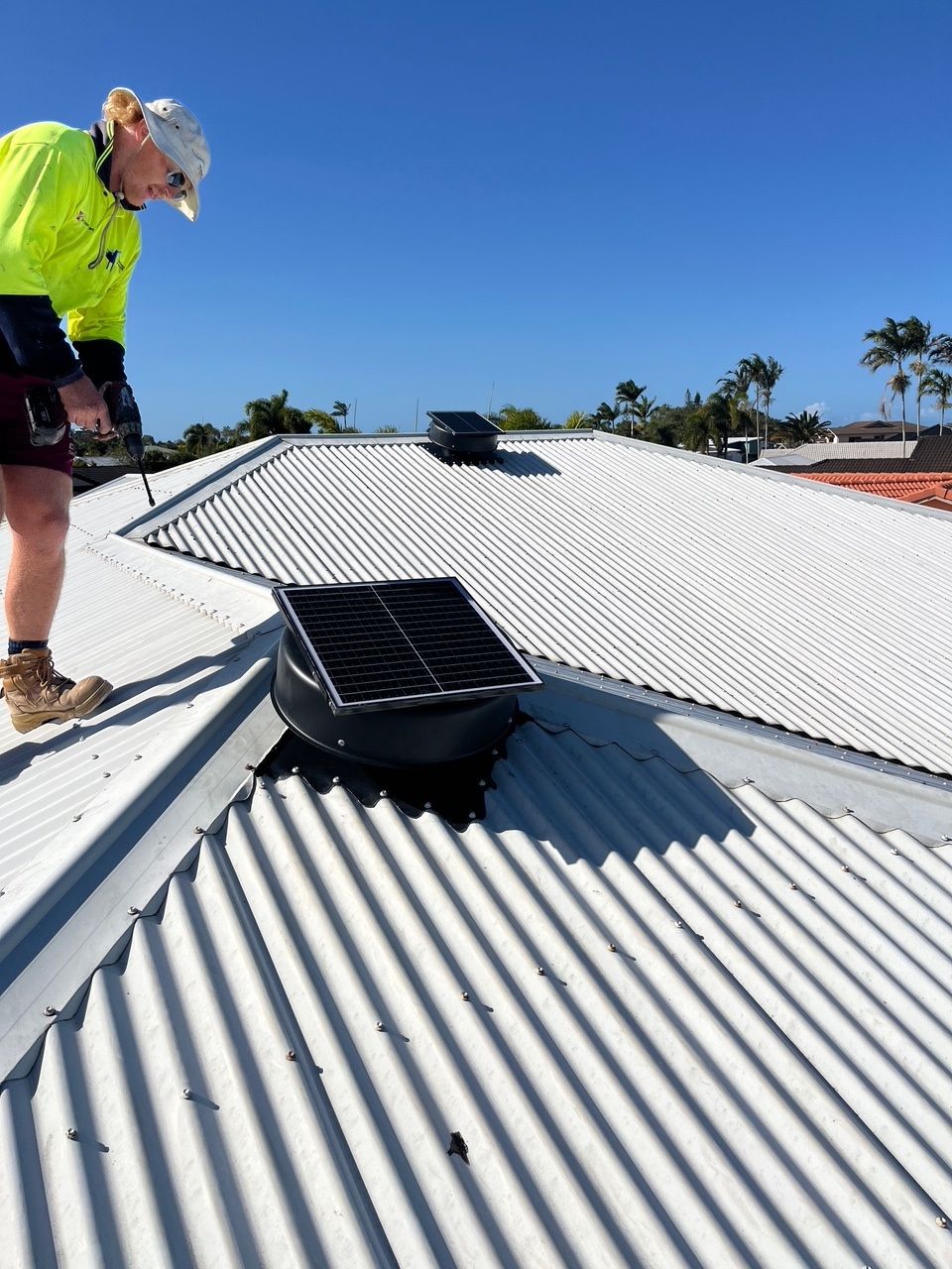 Worker inspecting a white corrugated metal roof with a black roof vent under a clear blue sky — Depinto Agencies In North Mackay, QLD
