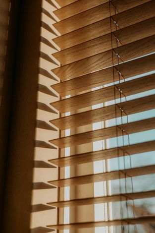 Sunlight streaming through beige window blinds, casting striped shadows on a wall.