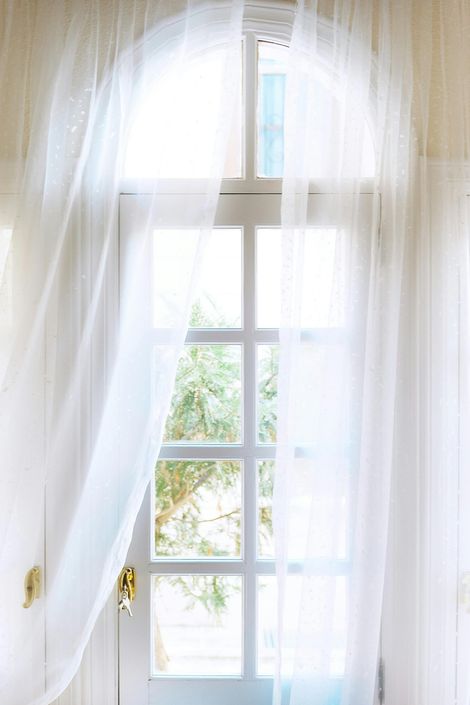 Sheer white curtains framing a bright window with soft daylight outside