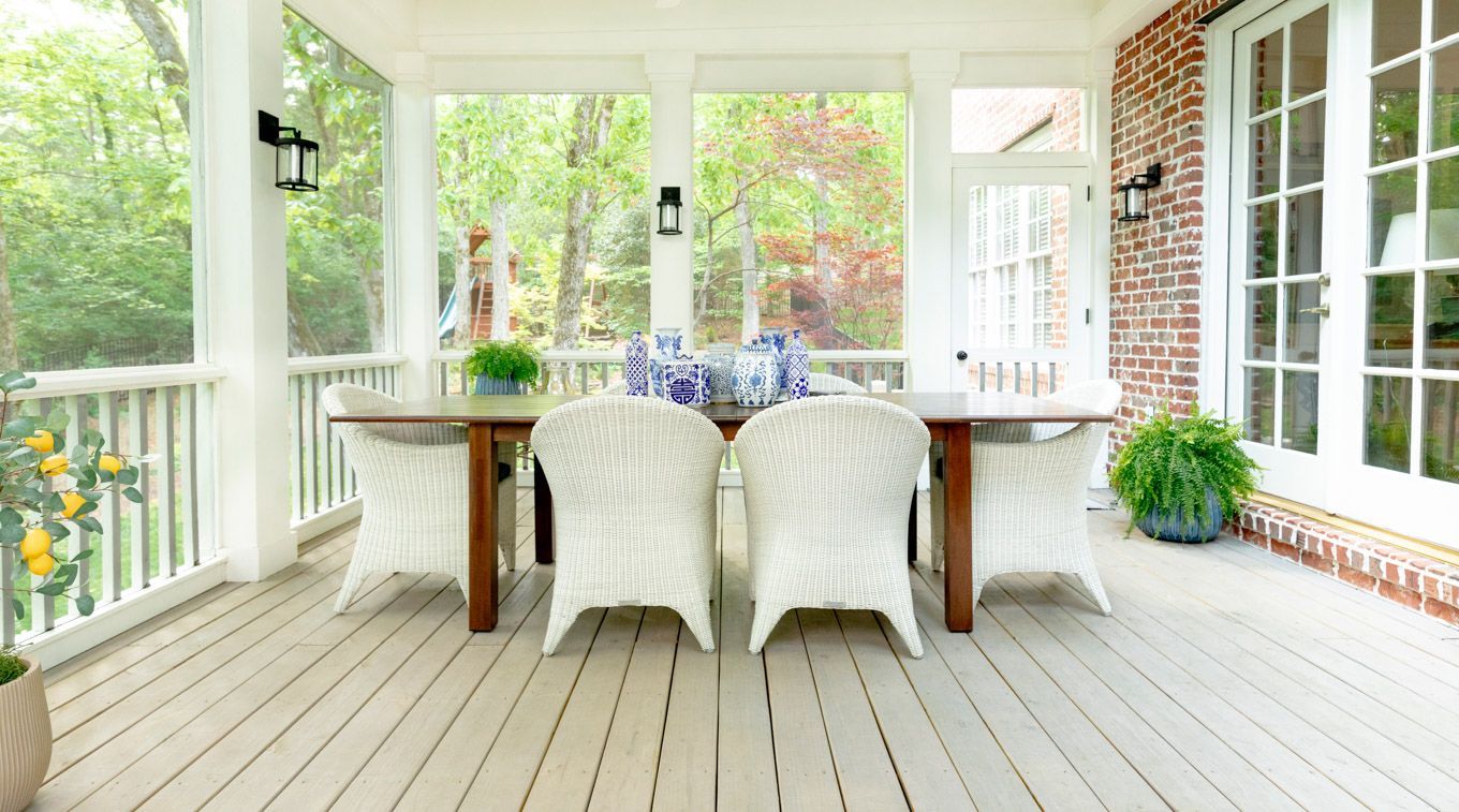 Bright screened porch with white wicker chairs, wooden dining table, and potted plants on a deck