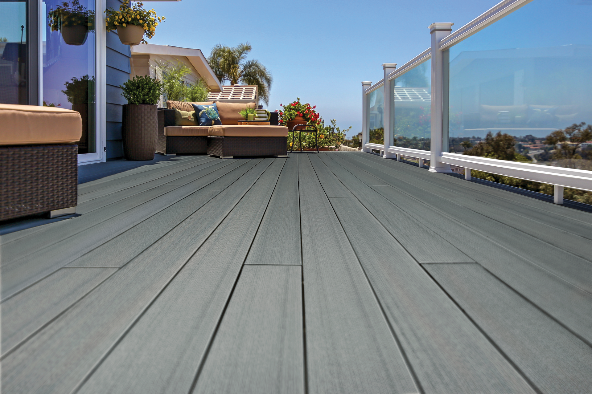 Spacious rooftop deck with gray planks, lounge chairs, potted plants, and glass railing overlooking the ocean