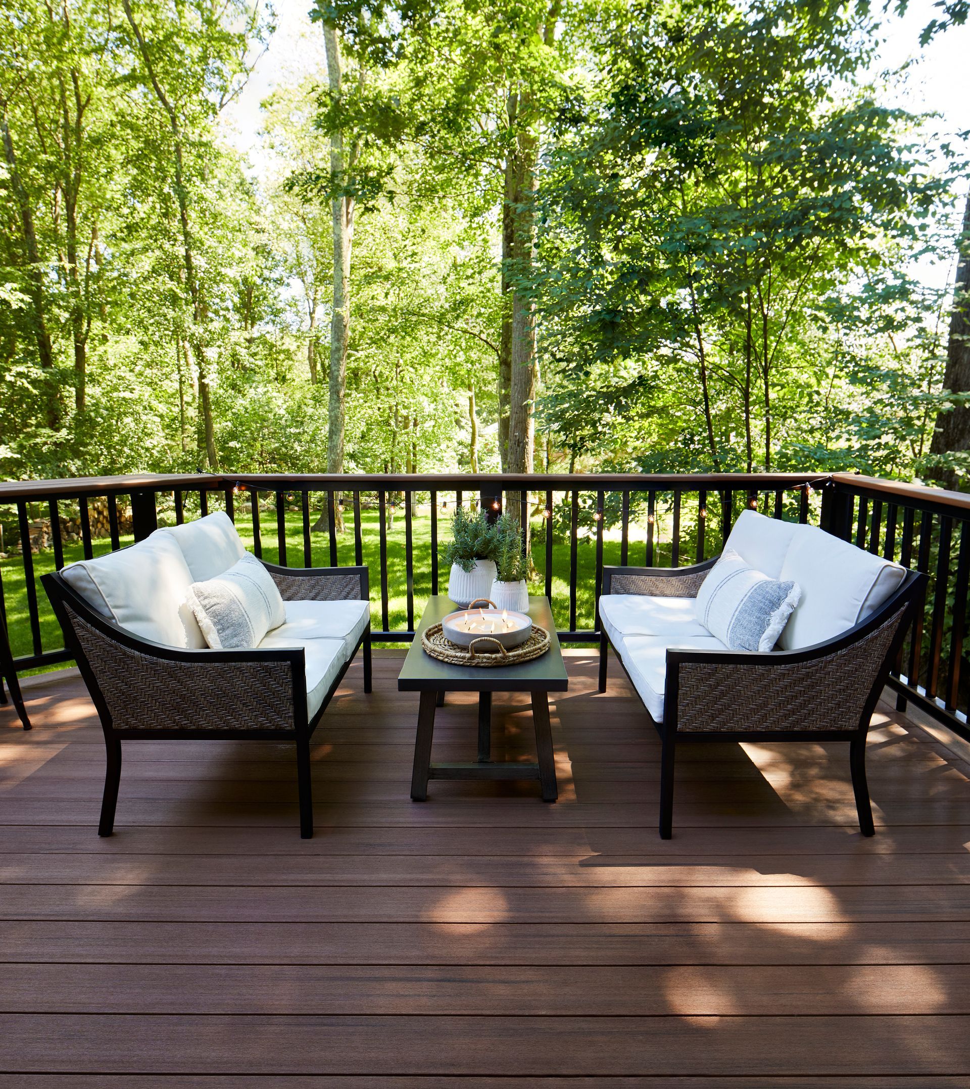 Wooden deck with two white cushioned chairs and a small table overlooking a green forest.