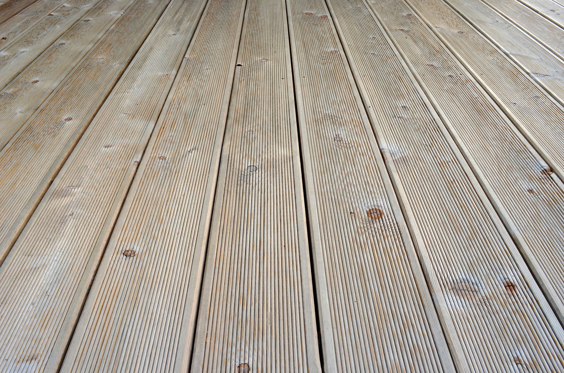 Weathered wooden deck boards with diagonal grooves and scattered small brown stains