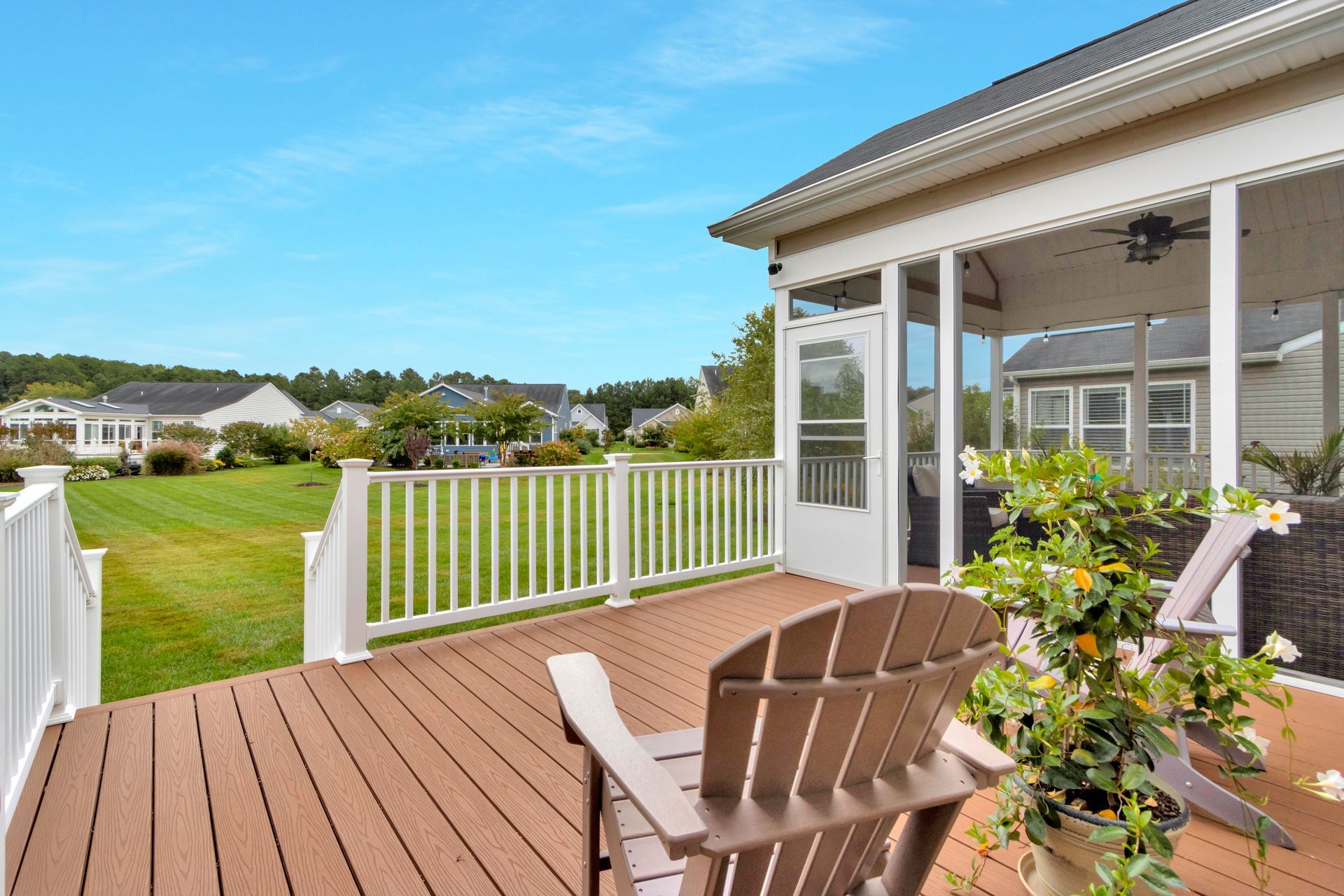 Sunlit deck with white railing, wicker chairs, and a view of a green neighborhood.