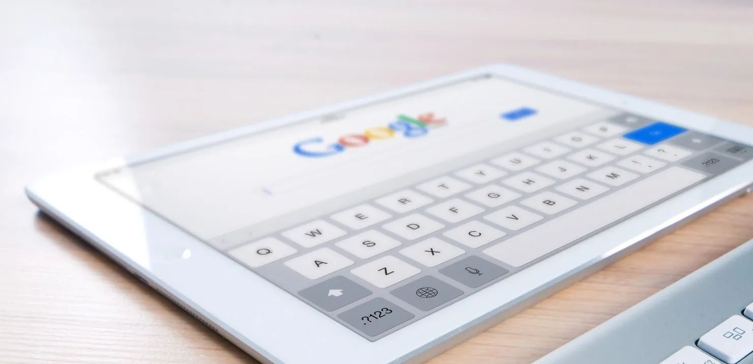 A tablet is sitting on a wooden table next to a keyboard.