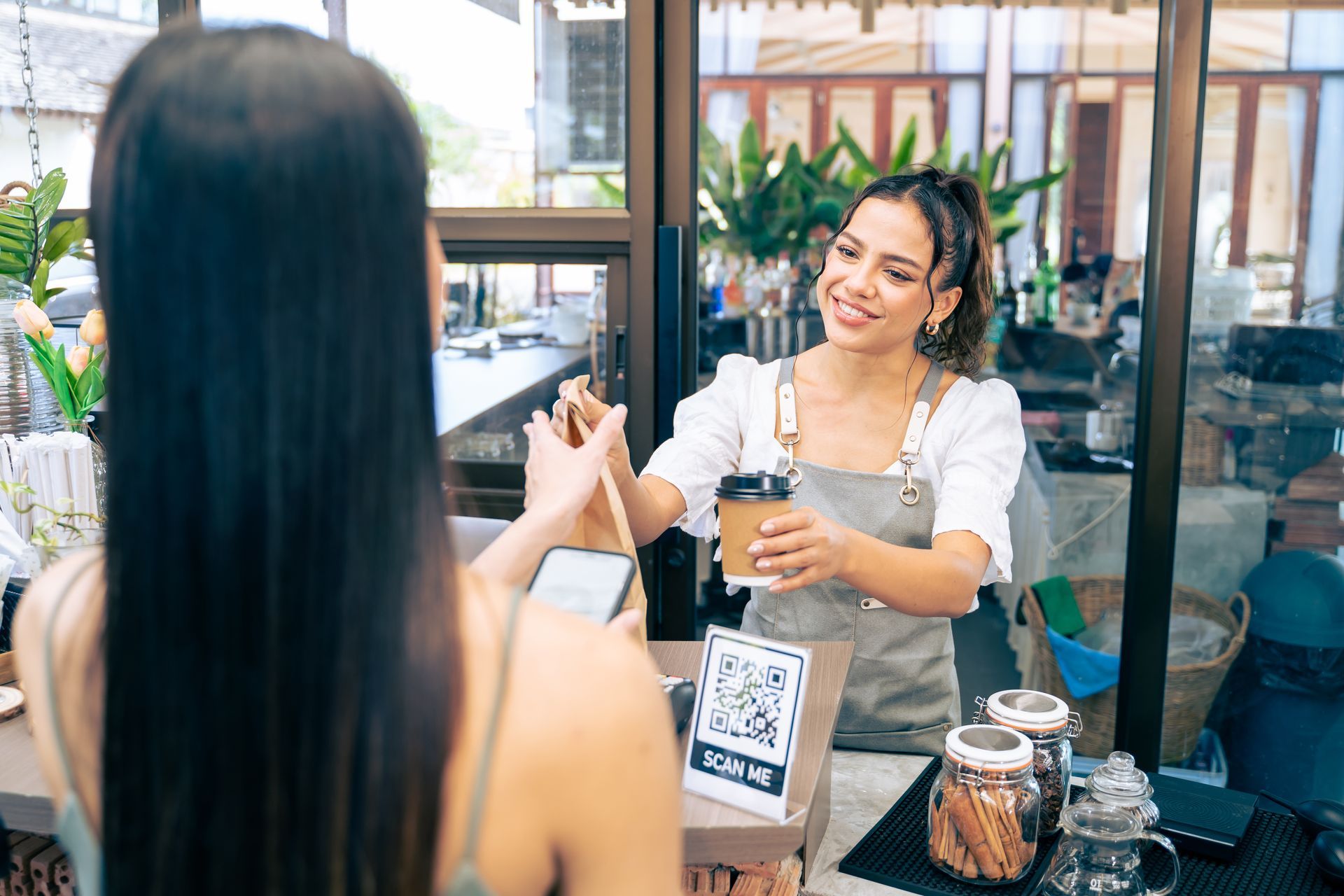 Woman pays for coffee via phone at a cafe counter; barista smiles, handing her a cup.