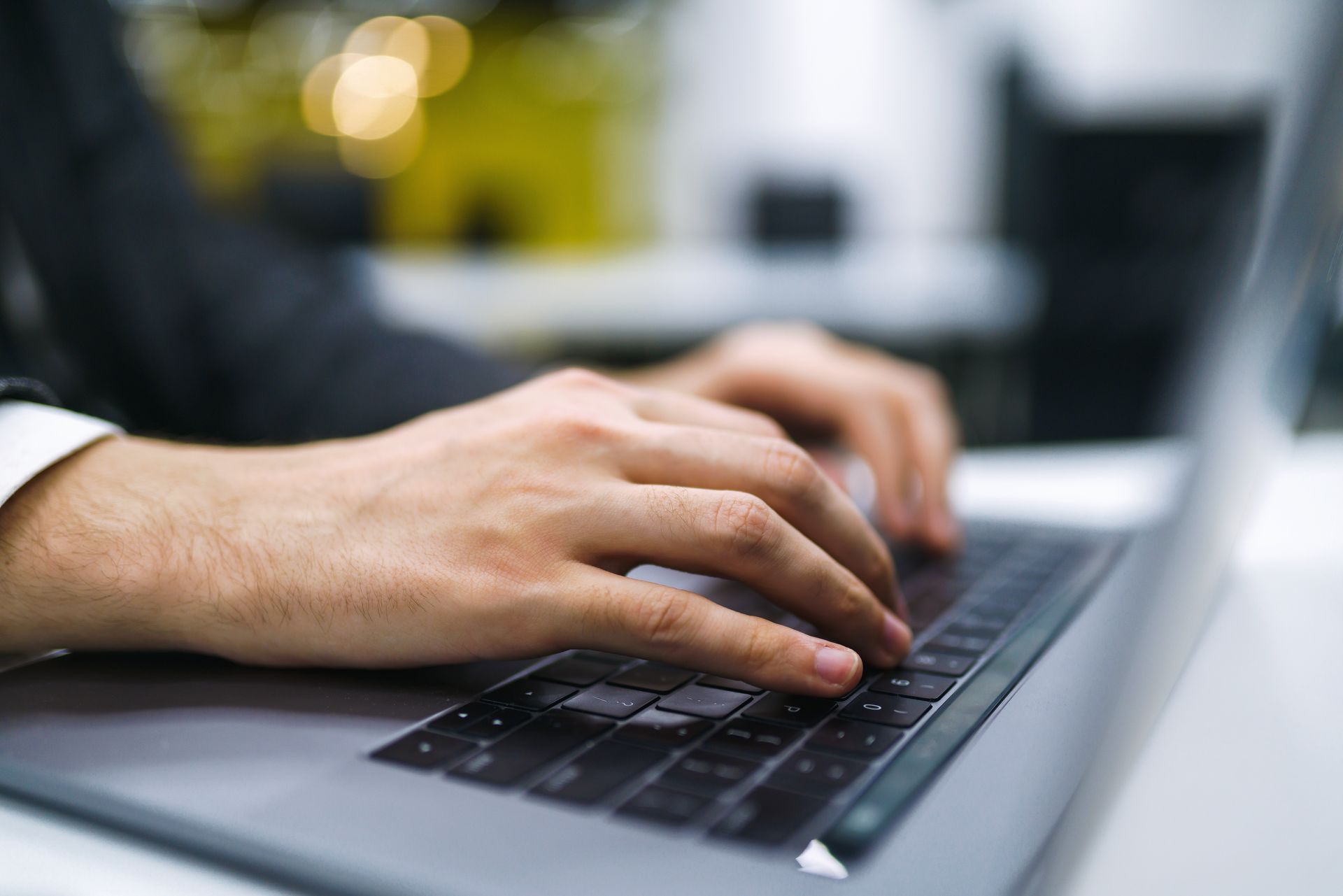 Person typing on laptop with both hands, likely in an office setting.
