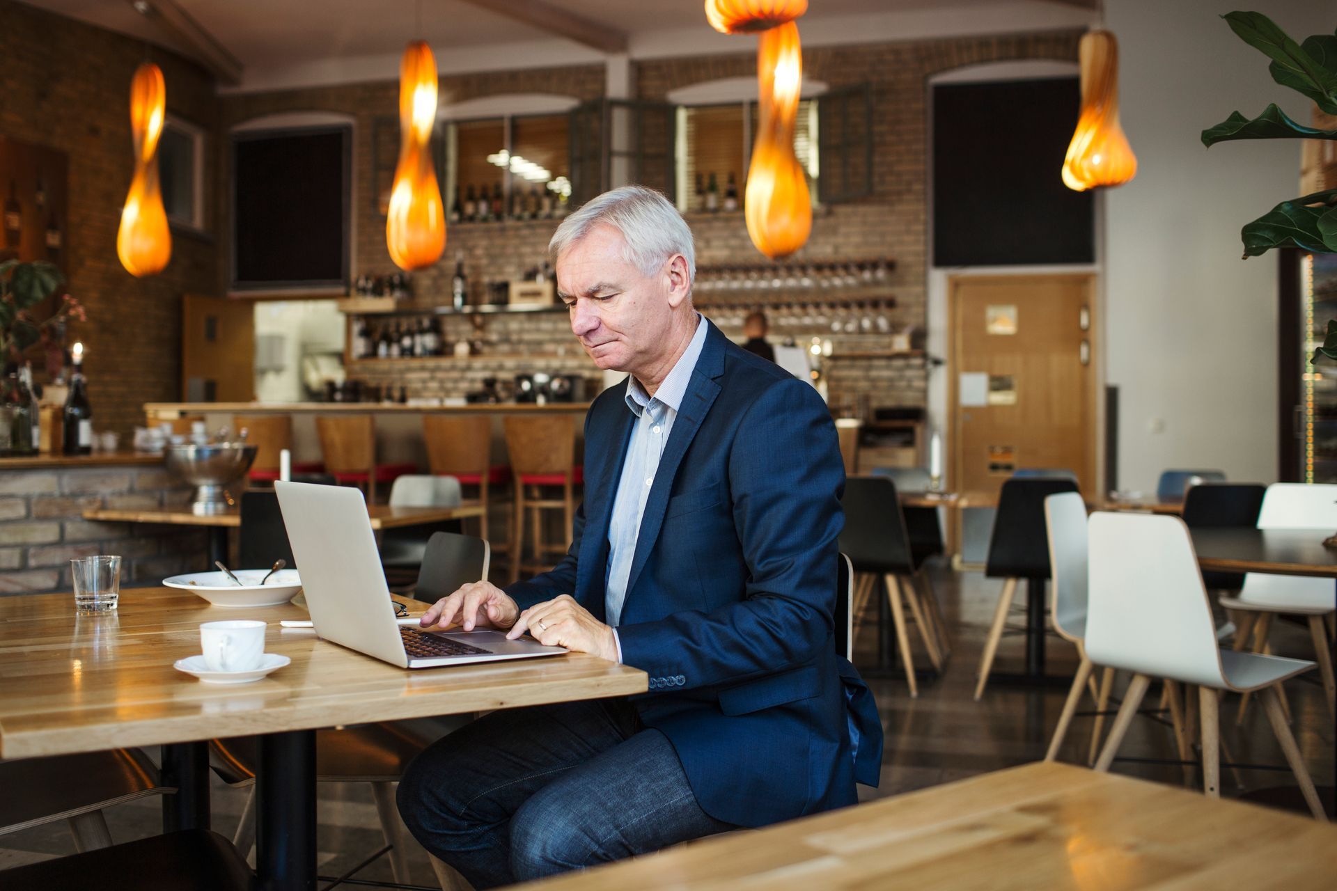 Man in suit typing on laptop at restaurant table, smiling, warm lighting.