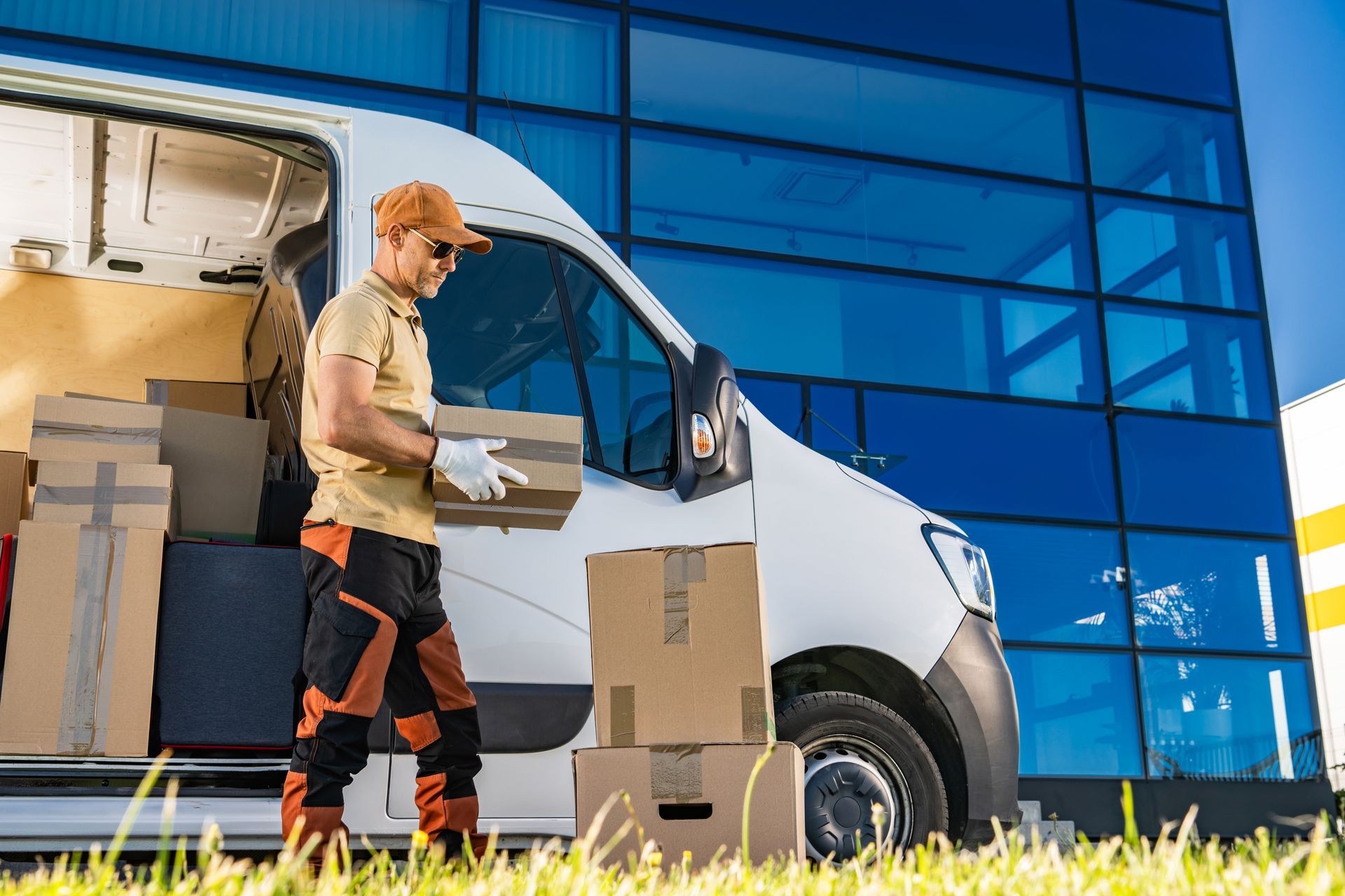 Delivery person loading boxes from a white van near a glass building.