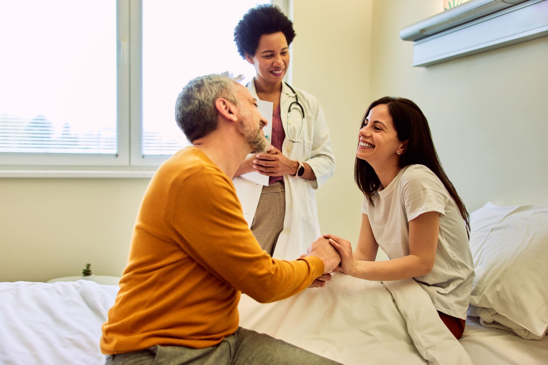 Doctor smiles at a couple, holding hands in a hospital room.
