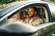Family smiles inside a car, driving on a sunny day.