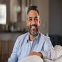 A man with a beard is sitting on a couch and smiling at the camera.