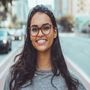A woman wearing glasses is smiling for the camera on a city street.