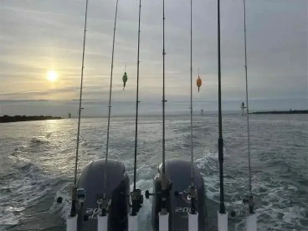 Fishing rods on a boat at sunrise over calm water, with two buoy markers in the distance.