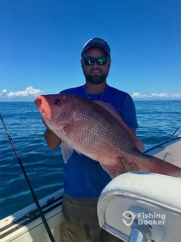 Man on a boat holding a large pink fish on a sunny blue ocean