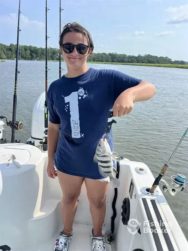 Person on a boat holding up a fish, wearing sunglasses and a navy shirt on a sunny lake.