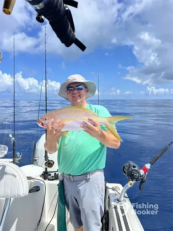 Person on a boat holding a colorful fish on calm blue water under a cloudy sky