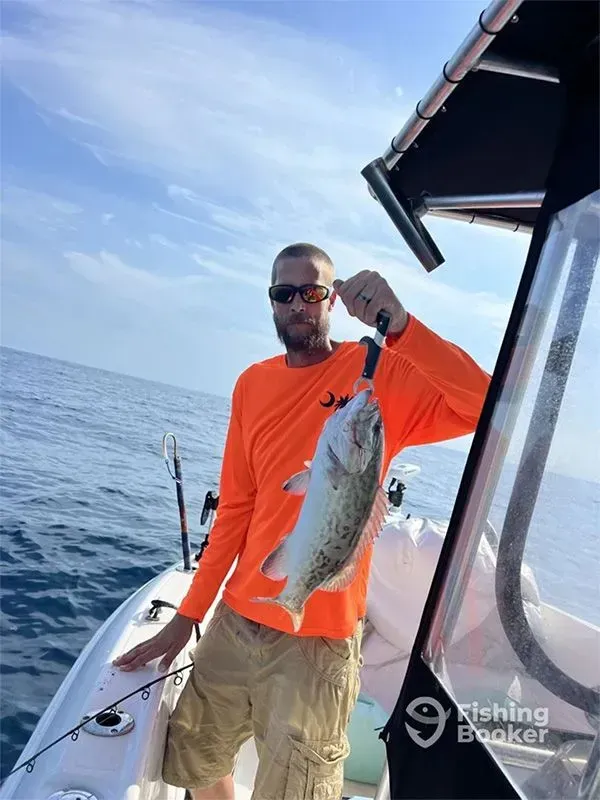Man on a boat holding up a large fish over the water, wearing a bright orange shirt and sunglasses.