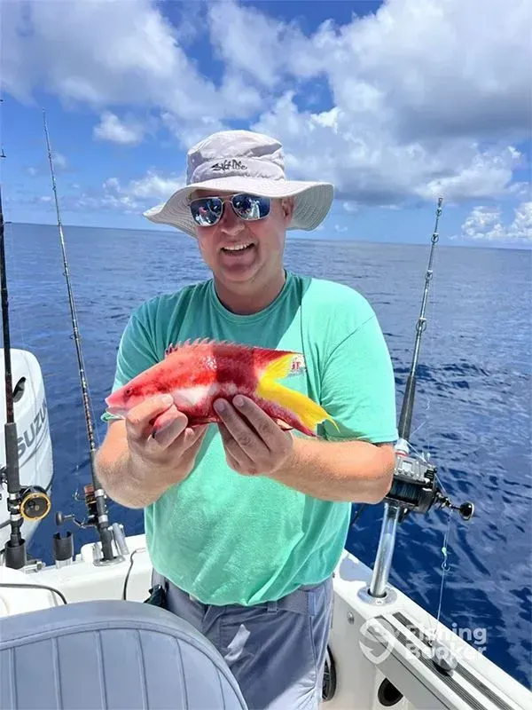 Smiling man on a boat holding a colorful red-and-yellow fish at sea