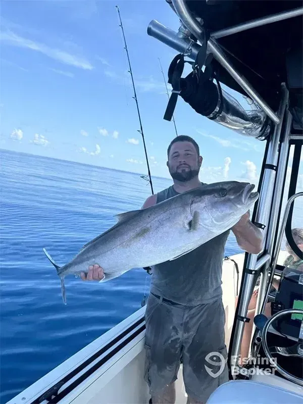 Man on a boat holding a large silver fish over calm blue ocean waters