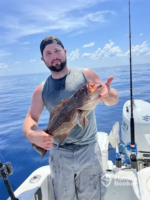 Man on a boat holding a large fish, with fishing rods and calm ocean behind him.
