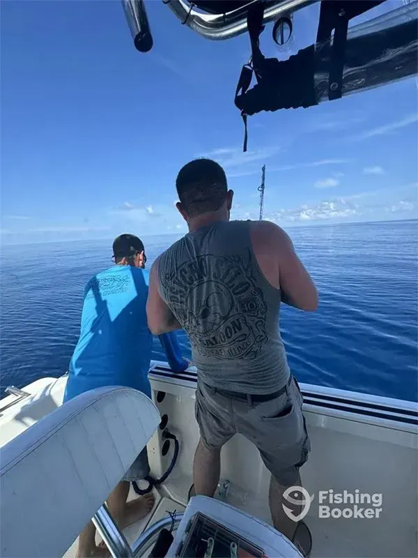 Two people fishing from a boat on a sunny ocean, with blue sky and open water ahead.