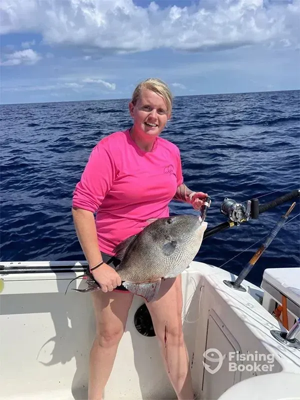 Person on a boat holding a large fish on the ocean under a blue sky